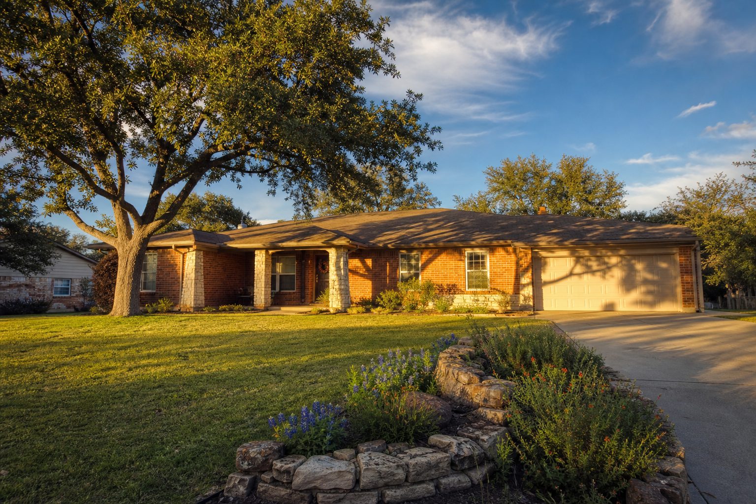 Traditional red brick ranch home in Springtown with mature oak trees and concrete driveway at golden hour.