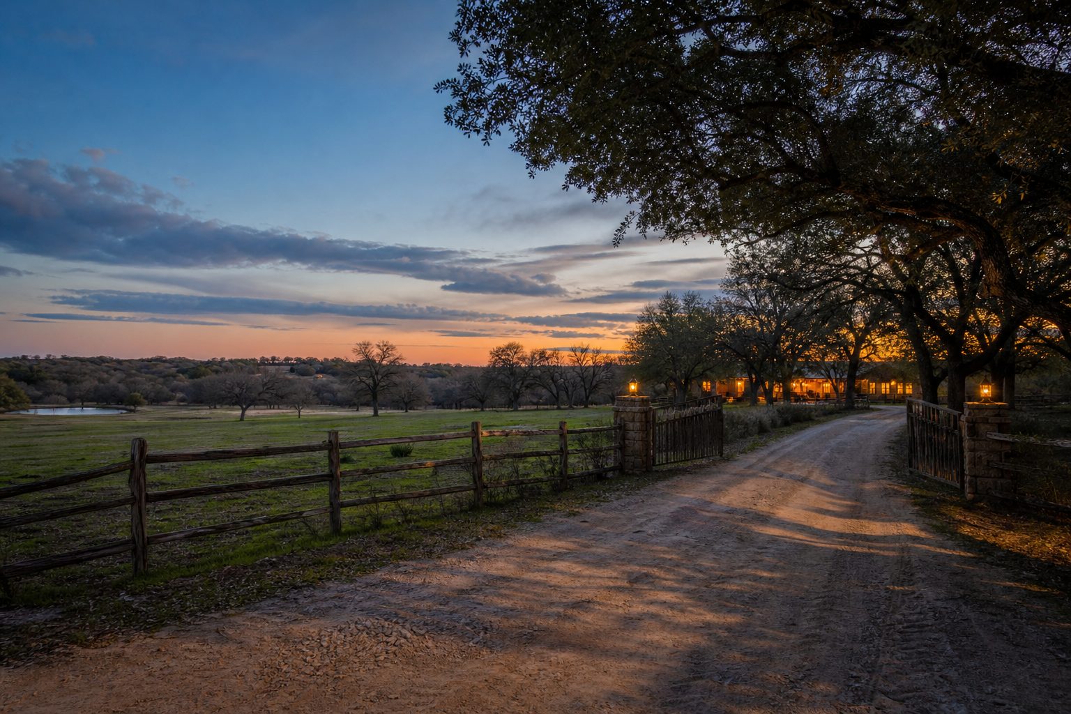Unpaved county ranch road bordered by mature oak trees and weathered fencing at dusk in rural Parker County.