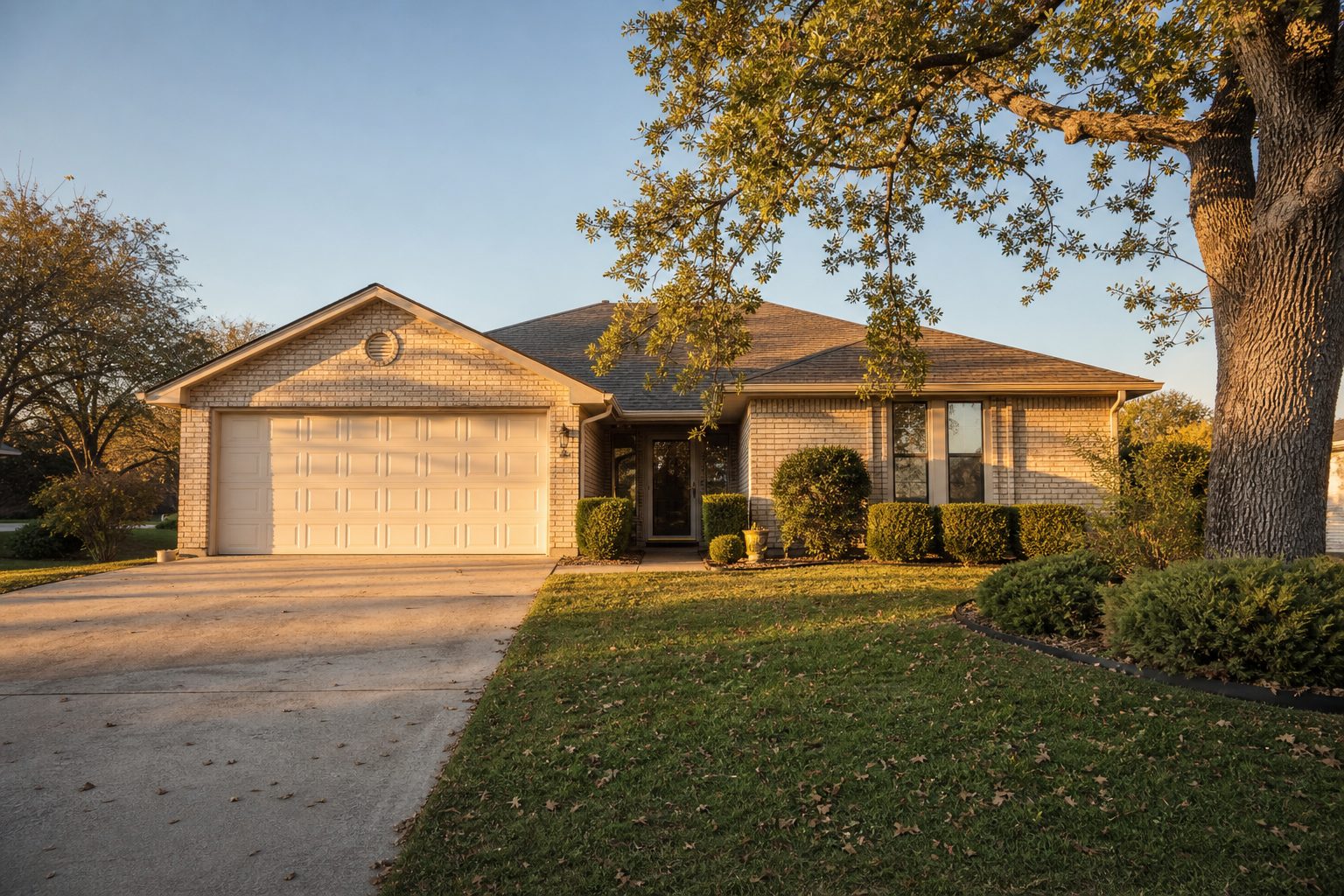 Single-story brick ranch home with mature tree and neatly trimmed yard in Graham, Texas residential neighborhood.