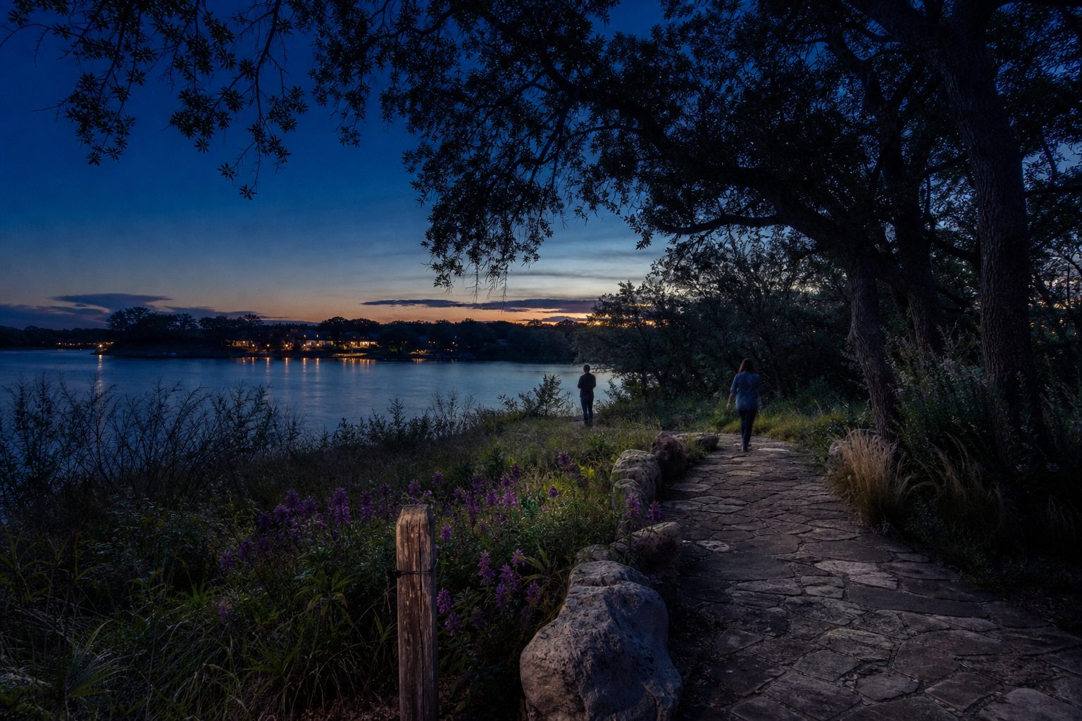 Twilight scene at Dutch Branch Park overlooking Benbrook Lake with walking trail, distant waterfront homes glowing at dusk.
